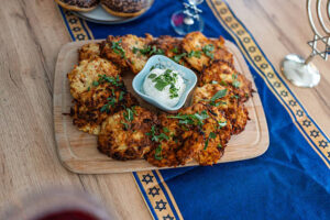 Potato latkes served with sour cream and herbs on a wooden board.