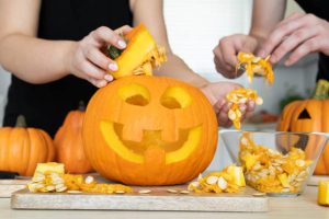Hands hollowing out a carved jack-o'-lantern