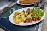 Scrumptious breakfast featuring scrambled eggs, fresh salad, and a baguette on a white plate.