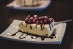 Slice of cheesecake topped with berries and chocolate drizzle on a plate.