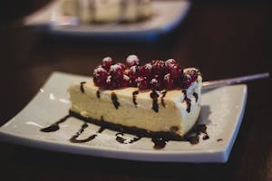 Slice of cheesecake topped with berries and chocolate drizzle on a plate.