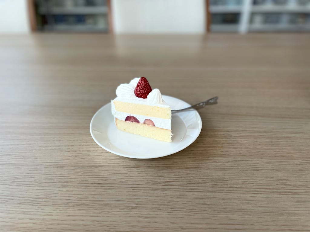 Sliced strawberry shortcake with whipped cream on a white plate, photographed indoors.