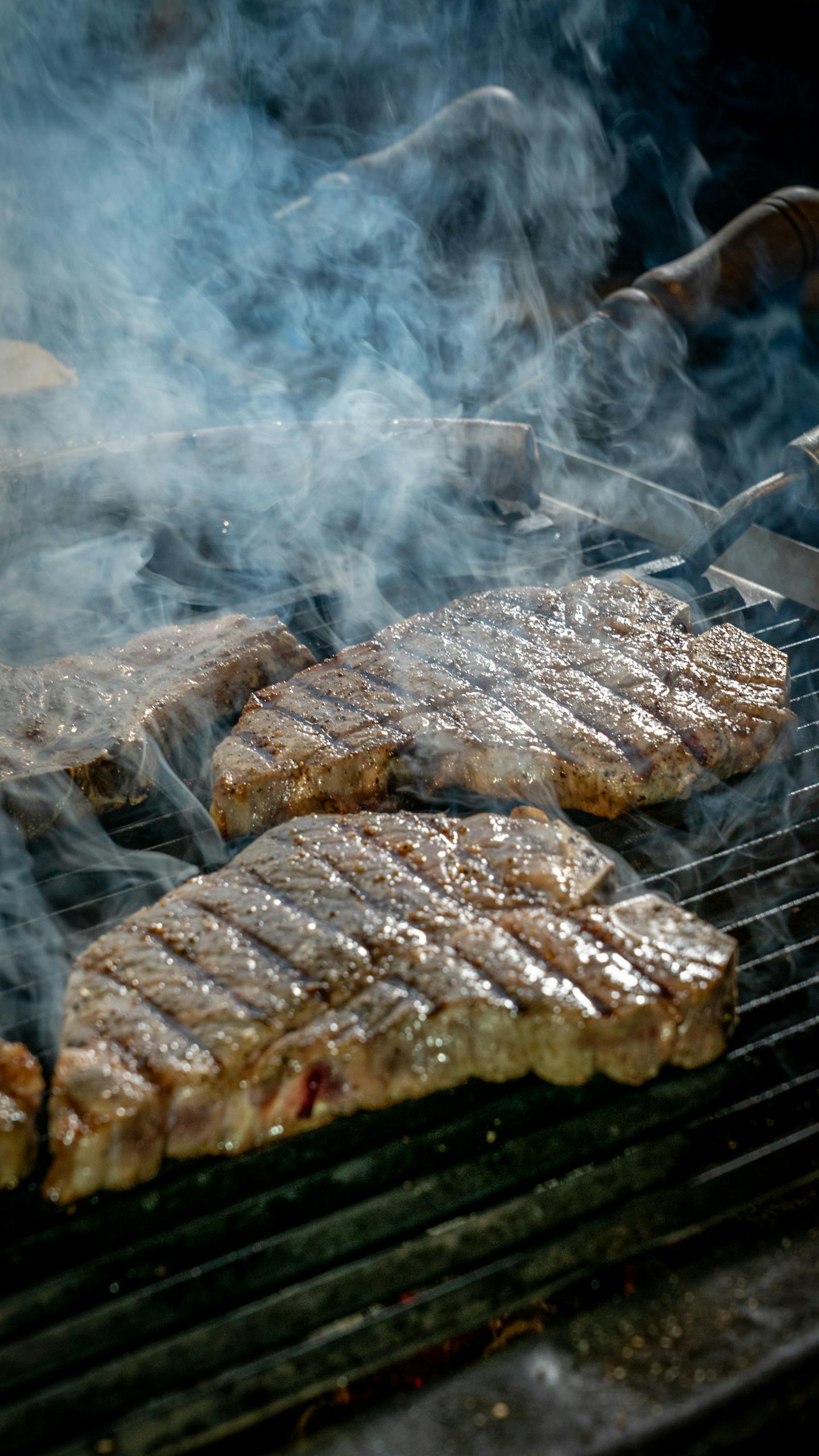 T-bone steaks sizzling on a smoky grill, perfect for a BBQ theme.