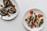 Tasty bruschetta topped with anchovies, arugula, and olives on white plates.