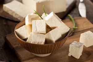 Cubed tofu in a wooden bowl on a cutting board