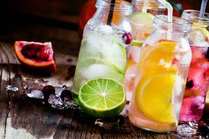 Glass bottles of citrus drinks with ice on a dark wooden surface