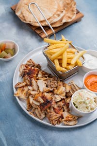 Top view of a Middle Eastern meal with grilled chicken, fries, and dips, perfect for lunch or dinner.