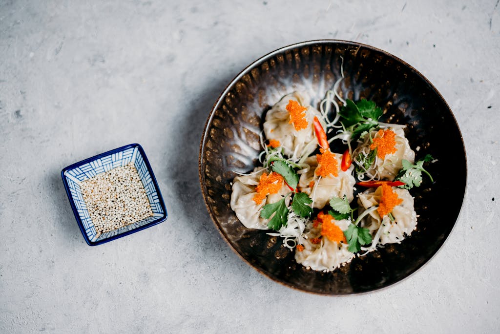 Top view of Asian dumplings garnished with roe and cilantro, served with sesame seeds.