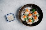 Top view of Asian dumplings garnished with roe and cilantro, served with sesame seeds.