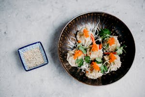 Top view of Asian dumplings garnished with roe and cilantro, served with sesame seeds.