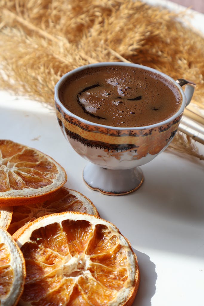 Warm coffee in vintage cup with dried orange slices on rustic background.