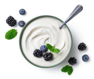 Top view of a bowl of yogurt with blueberries, blackberries, and mint leaves, with a spoon.